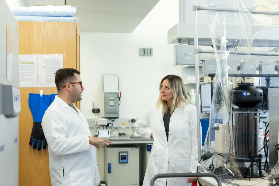 Two researchers discussing their work beside laboratory equipment