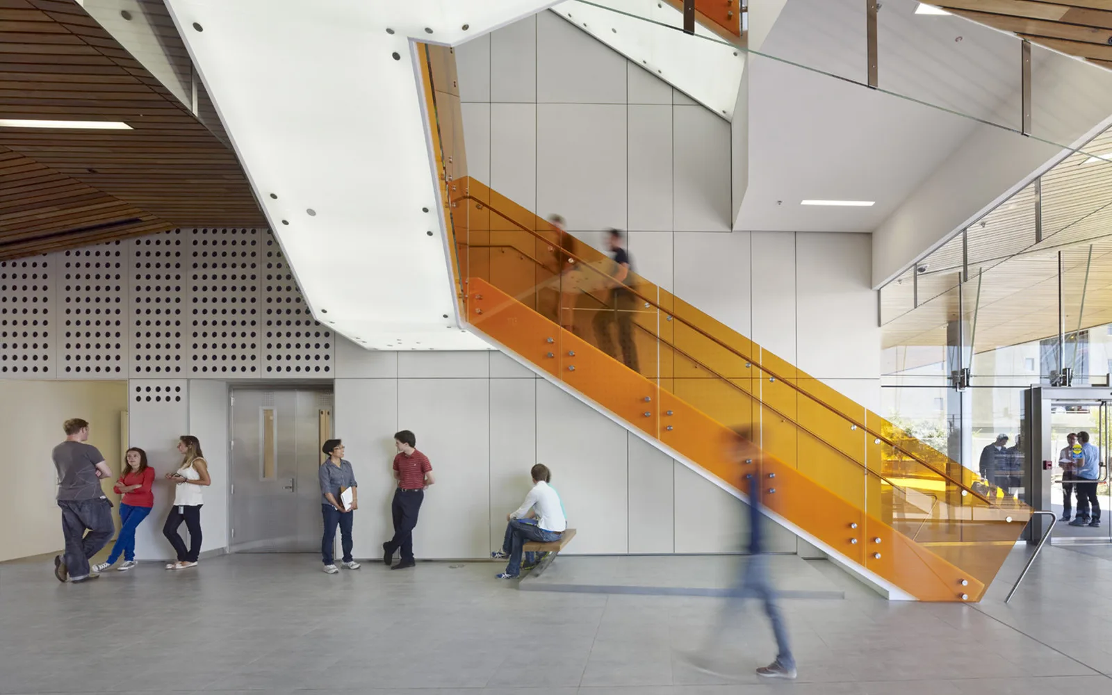 People gathering in the bright IGI atrium beside its orange staircase
